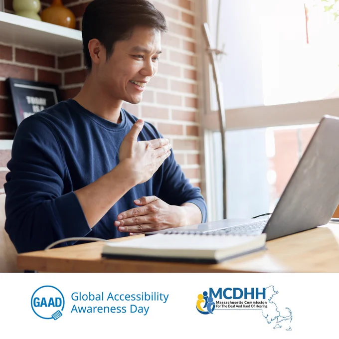 Asian man in a blue shirt smiles while communicating using sign language during a video chat on his laptop. GAAD and MCDHH logos appear at the bottom of the image.
