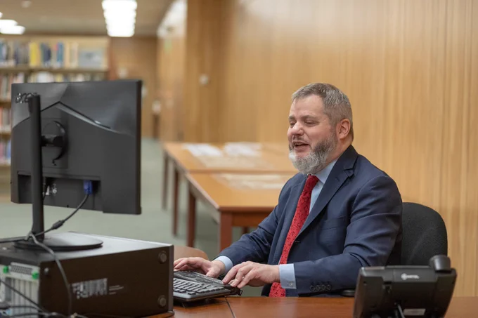 Federationist Chris Danielsen sits at a desktop computer while typing on a Braille device.