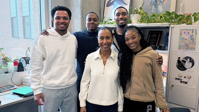 Tamara Markey stands smiling in the center of four Purdue Engineering students inside her office in Lambertus Hall, the group posing together with arms around each other in a warm, candid moment.