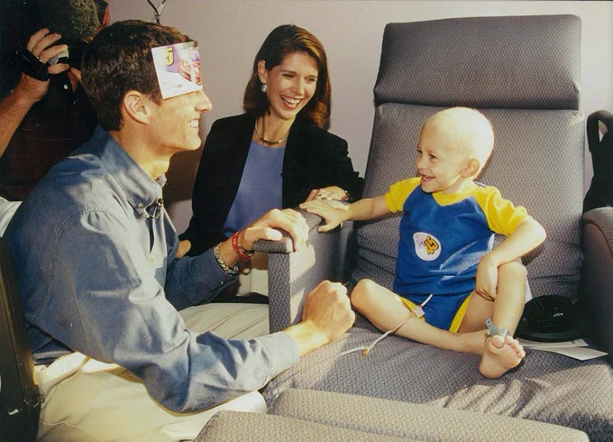 Adam Petty spending time with a child in the hospital. They are both smiling as Adam has a paper stuck to his forehead.