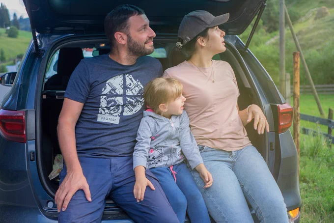A family sits in a car trunk, enjoying an outdoor adventure in a scenic countryside.