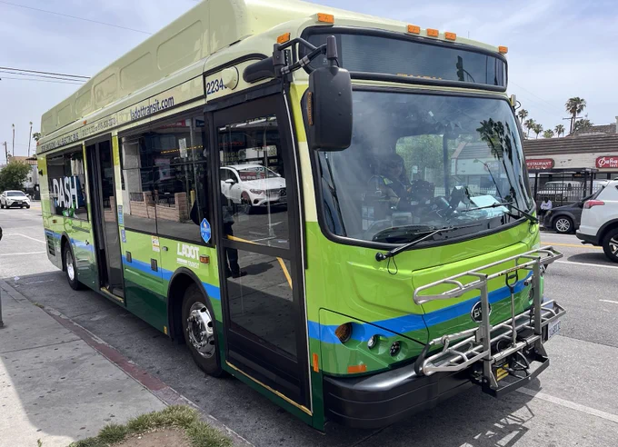 Bright green and blue DASH public transit bus parked at a city street curb with open front door and bike rack on the front.
