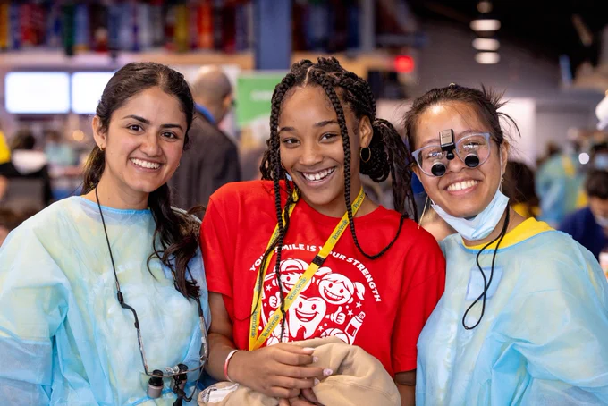 Two dental students and a child stand together and smile for a photo.