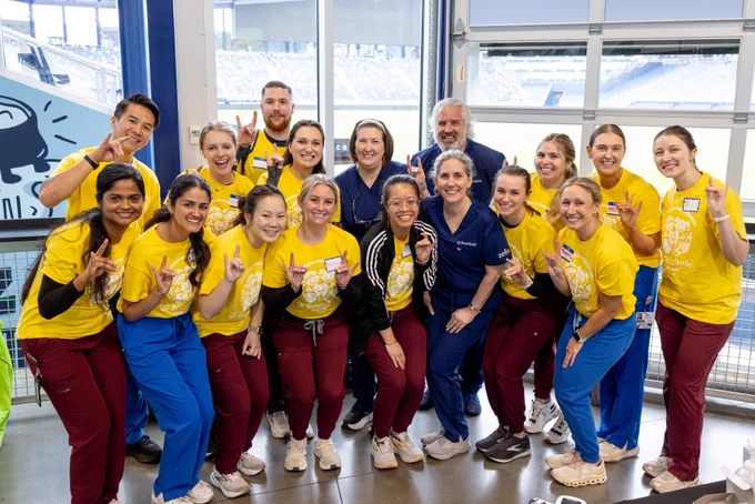 17 dental students and faculty pose for a photo together, wearing matching yellow shirts.