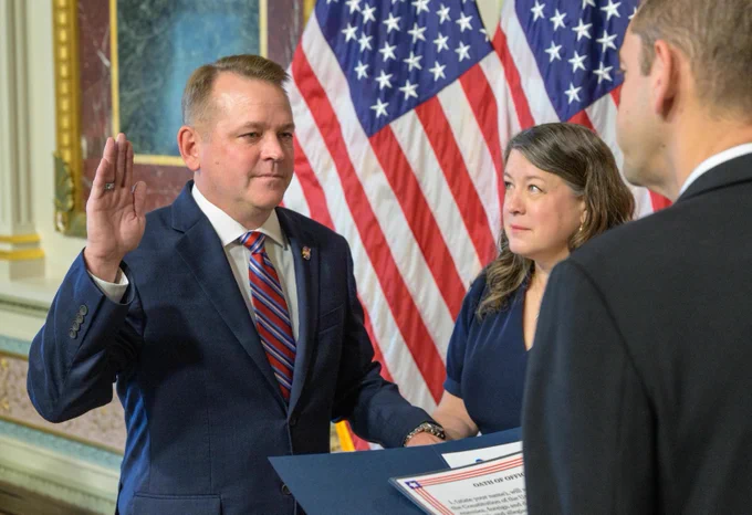 Matt Anderson, the 16th Deputy Administrator of NASA, stands with his right arm raise next to his wife, Christine. Behind him, two American flags stand. Credit: NASA/Bill Ingalls
