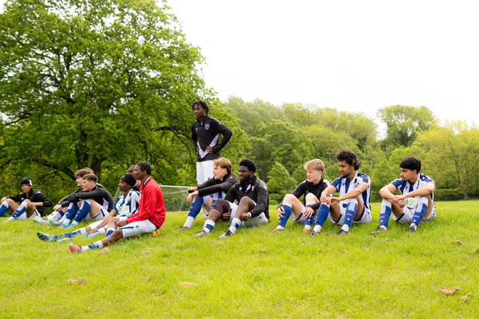 Post 16 Players sitting on the grass, watching a match.