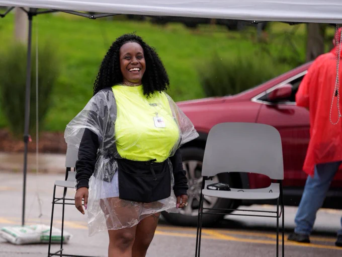 An admission worker posing for a photo. She is smiling while wearing a bright neon yellow shirt and a plastic rain coat.