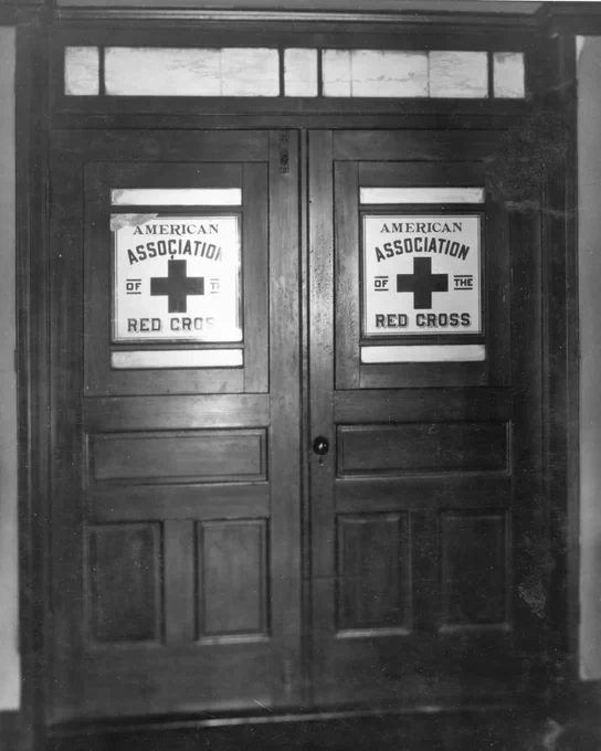 A wooden double door featuring two signs with the text "American Association of the Red Cross" above a large red cross symbol.