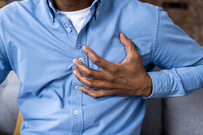 Man in blue shirt clutching his chest, indicating possible chest pain or discomfort.