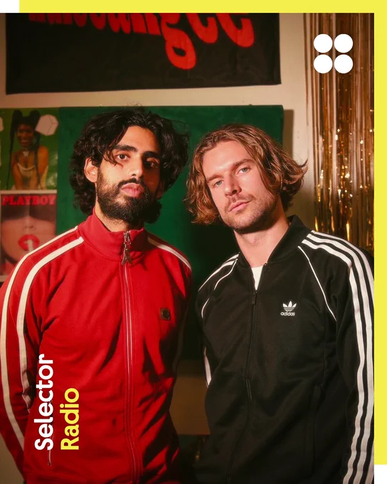 Scottish musical duo KuleeAngee pose indoors wearing retro-style tracksuit  jackets, one in red and one in black, against a warm-toned backdrop with posters and metallic streamers. The Selector Radio logo is in the bottom left corner, while the British Council logo (four circles) is in the top right. The border is yellow. 