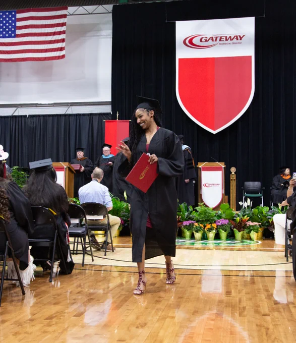 Graduate in cap and gown holding diploma folder walking across stage at Gateway Technical College ceremony.