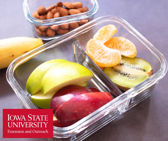 Glass container with sliced green and red apples, kiwi, and orange slices