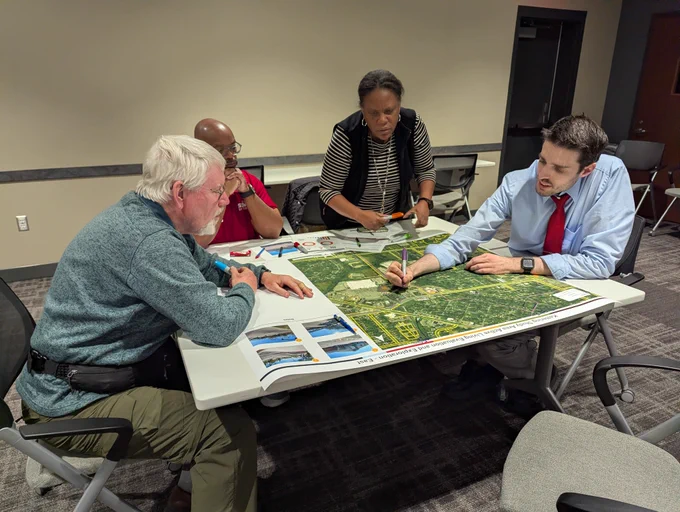 Members of a community gathering around a table, in discussion, looking at a map. 