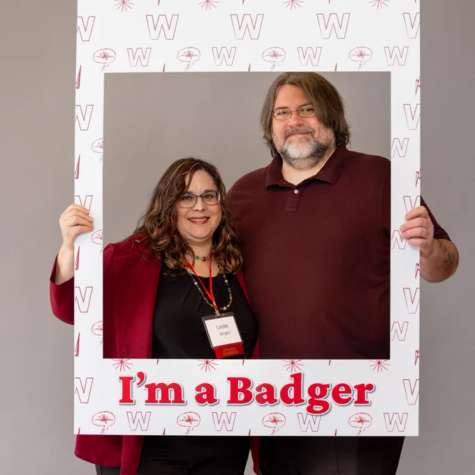 Returning adult student Leslie Wright and her husband standing inside a cutout photo frame that says, "I'm a Badger."