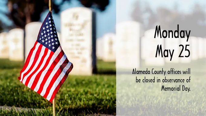 American flag planted in a cemetery with Memorial Day closure notice for Alameda County offices on May 25.