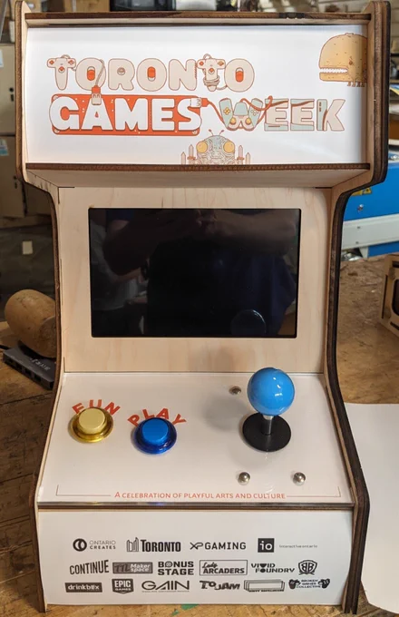 Vintage arcade machine featuring a colorful 'Toronto Games Week' sign and joystick controls on a wooden cabinet.