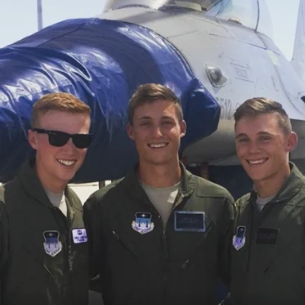 Griffin Jax smiles alongside two other men during his time at the United State Air Force Academy. They are all wearing Air Force uniforms and standing in front of a plane.
