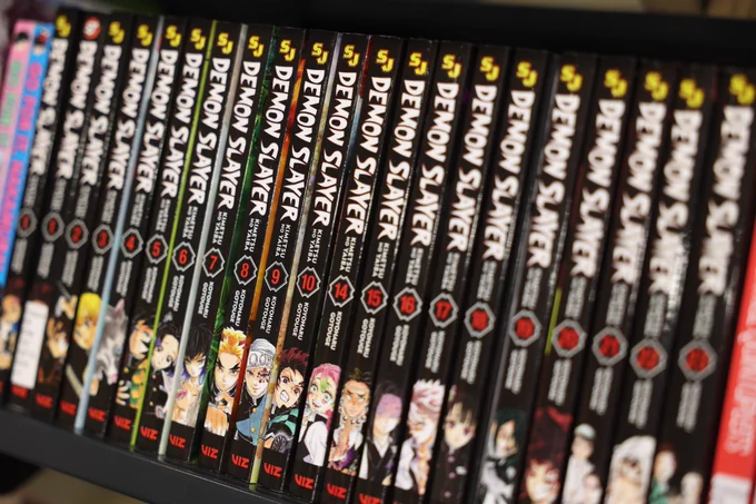 Close-up photos of manga and graphic novel shelves in a library collection, featuring titles including Hellsing, Demon Slayer, Attack on Titan, and Assassination Classroom.