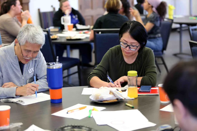 Pictured is a photo of two U T A Libraries staff members writing on a piece of paper while sitting at a table at the Lunch and Learn event on May 21.