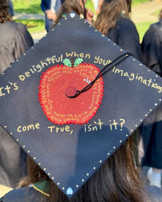 A graduation cap decorated with a sequined apple design and the phrase "It's delightful when your imaginations come true, isn't it?".