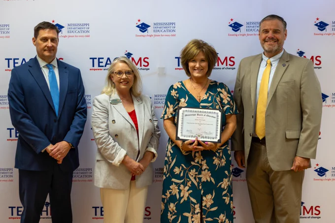 The Rural Teacher of the Year Award recognizes and honors outstanding teachers who have made significant contributions to rural education statewide. This year, Melanie Davis-Hardy was selected from four finalists, each representing one of Mississippi’s congressional districts. She is also a member of the Mississippi Teacher Advisory Council.
As the 2026 Mississippi Rural Teacher of the Year, she will serve as an ambassador for rural education and represent Mississippi at the National Rural Education Association (NREA) Conference, where the nation’s top rural teacher will be named.
 
The photo shows four people standing together, with one person holding a certificate.