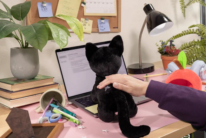 A photo of the Little Kitty plush in a pre-terrorized desk set, looking like it's about to climb onto somebody's laptop keyboard.