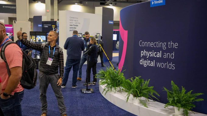 A man taking a selfie in front of a quote on a sign inside of the exhibit hall at Trimble Dimensions.