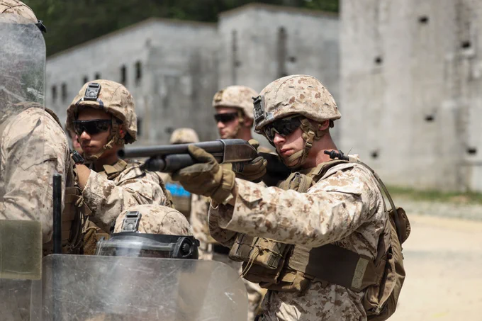 U.S. Marine Corps Lance Cpl. Joshua M. Aikman, a security force guard with 1st Platoon, Guard Company, Marine Barracks Washington, aims down the sights of his Mosberg 500 during civil disturbance training as part of Military Operations in Urban Terrain on Marine Corps Base Quantico, Virginia, May 13, 2026. Civil disturbance training teaches Marines how to employ non-lethal weapons and tactics, enabling them to de-escalate threats and control crowds with minimum force. MOUT provides Marines with the opportunity to refine their urban warfare tactics in a dynamic, real-world setting. Emphasizing speed, precision, and tactical coordination, the Marines worked through a series of challenging exercises, including room clearing, security maneuvers, and small unit tactics. (U.S. Marine Corps photo by Lance Cpl. Landon Heredia)\n\n