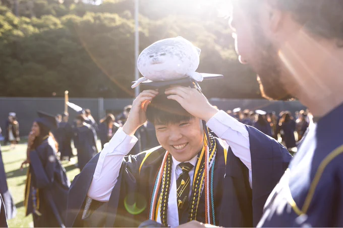 Thomas Yu smiles beneath a sun flare with a seal plush on his mortarboard. (Photo by Brittany Hosea-Small)
