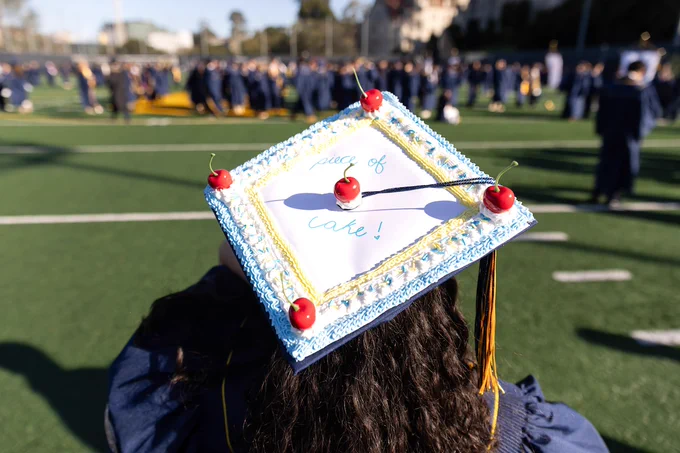A mortarboard decorated like a cake with blue frosting and cherries. Text: “Piece of cake!” (Photo by Brittany Hosea-Small)