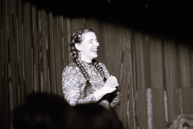 An in profile side on photograph of a woman laughing on stage.