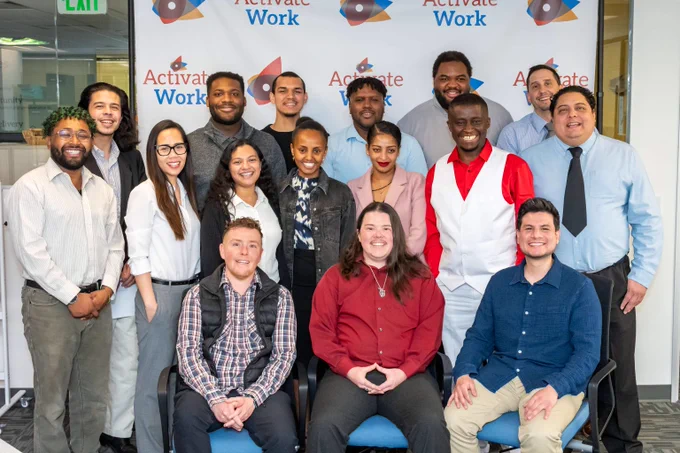 Diverse group of 15 smiling professionals posing in front of an ActivateWork branded backdrop in an office setting.