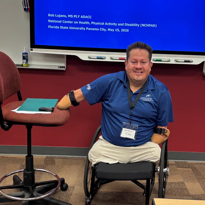 NCHPAD's Bob Lujano in front of a projection screen at the conference smiling for a photo.