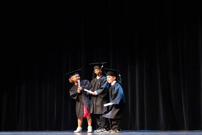 The three graduates from Barker ELC smiling at each other in their cap and gowns with diplomas in hand.