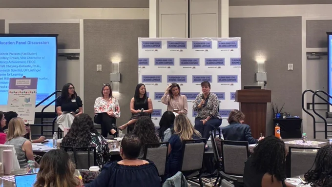 Five people conducting a panel in front of a crowd.