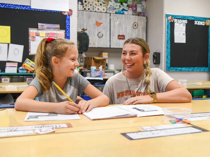 female teacher and female elementary student work on classwork at a table
