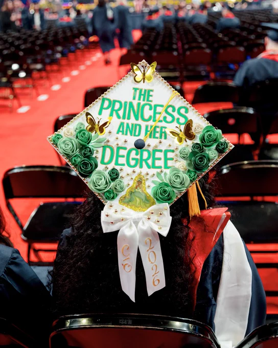 A grad cap with butterflies and green flowers that says “the princess and her degree”