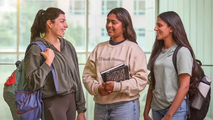 Three UTHealth Houston nursing school students wearing backpacks smile together on campus between classes. 