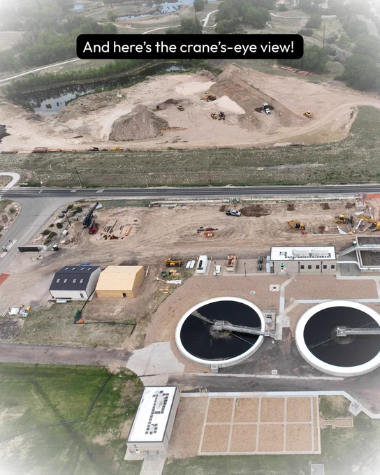 Aerial view of a construction site showing large circular structures and machinery, with earthworks in progress in the background. Text reads: And here's the crane's-eye view!