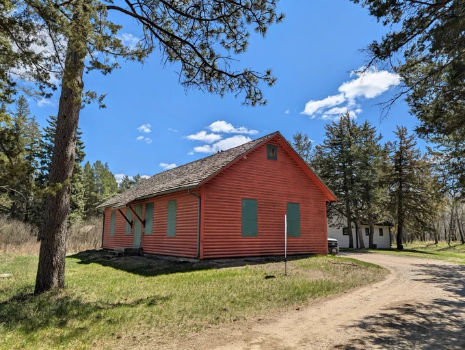 A modern photograph shows the red historic Forester’s Cabin nestled among tall pines in North Dakota. Forest Service photo by Scott C. Marvin.