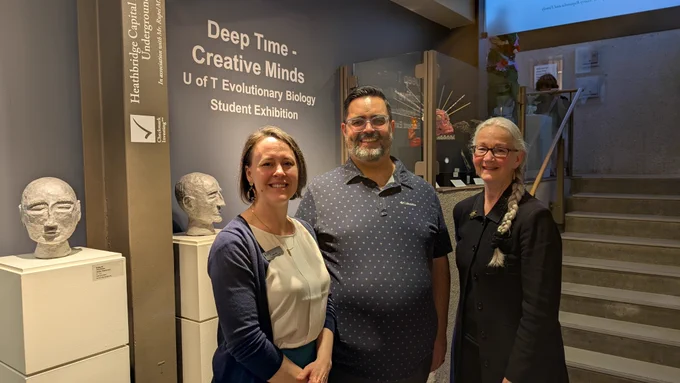 Three individuals stand in front of a display titled "Deep Time - Creative Minds: U of T Evolutionary Biology Student Exhibition" at the Headhunters Capital art gallery.