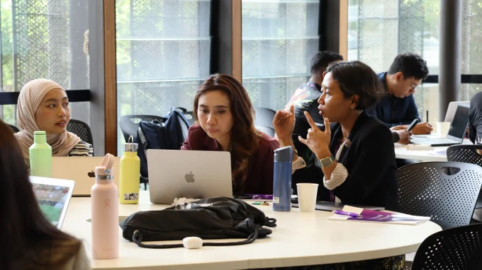 Small group of participants collaborating at a table with laptops and notebooks. 