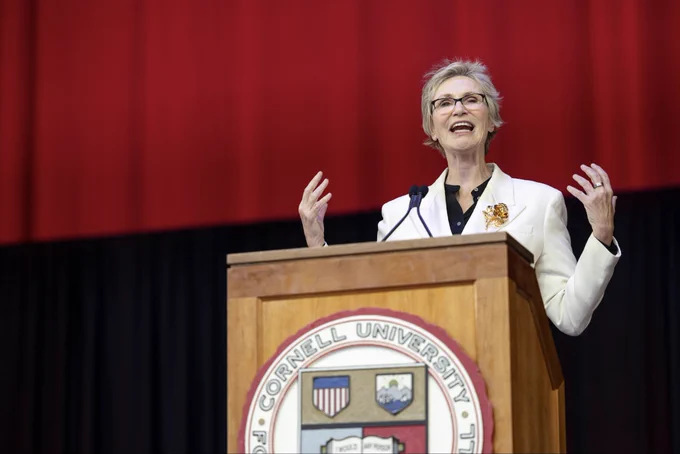 Jane Lynch stands at a podium bearing the Cornell crest at the 2026 Cornell Convocation.