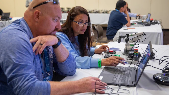 Two conference attendees work on a VEX CTE 6-Axis Arm and look at code on a laptop together.