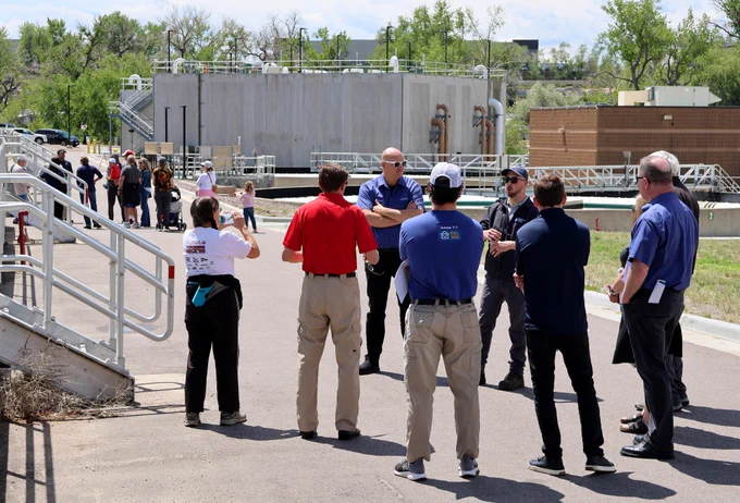 Group of people standing listening to a man lead a tour at a wastewater treatment facility with another group in the distance.