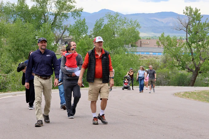 Group of 11 people walking up a long drive way with green trees in the background at a wastewater treatment plant.