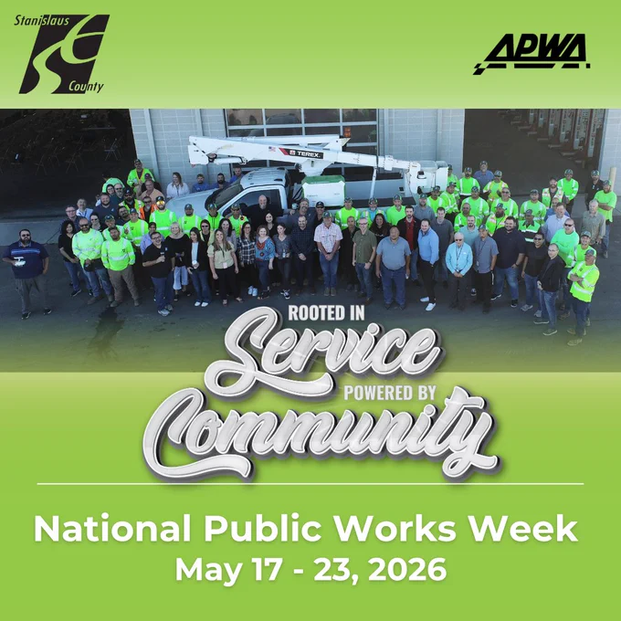 Promotional graphic for National Public Works Week 2026 featuring a large group photo of Stanislaus County public works employees gathered in front of a public works facility and utility truck. The design has a bright green background with the Stanislaus County logo on the left and the APWA logo on the right. Over the photo is the slogan “Rooted in Service, Powered by Community” in stylized lettering. Large white text at the bottom reads “National Public Works Week, May 17–23, 2026.”