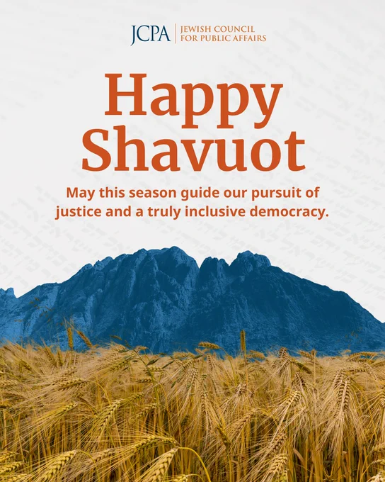 Shavuot greeting graphic from JCPA featuring the text: “Happy Shavuot” in large orange lettering, followed by the message: “May this season guide our pursuit of justice and a truly inclusive democracy.” The background includes faint Hebrew text, a blue-toned mountain landscape, and a golden wheat field in the foreground, symbolizing the harvest holiday. JCPA branding appears at the top.