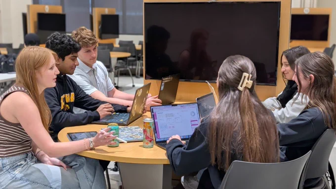 Six students sit around a table working on laptops together in a University of Iowa classroom and collaboration space.