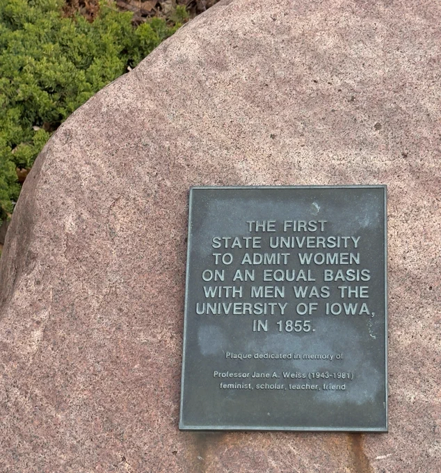 Plaque on a large rock commemorating the University of Iowa as first state university to admit women equally in 1855.
